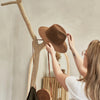 Close-up lifestyle shot of a person hanging a brown hat on the natural wood branch coat hook highlighting the functional organic design