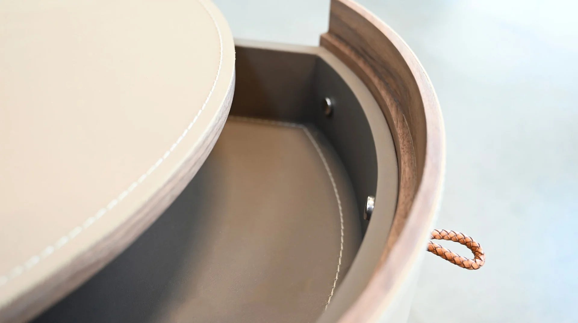 Front view of the Neru nightstand featuring a circular 3-drawer silhouette wrapped in light grey leather with contrasting top stitching