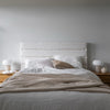 Lifestyle perspective of the sand upholstered bed styled with layered pillows and a textured throw blanket