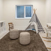 Lifestyle perspective of two yarn poufs used as floor seating in a modern kids' playroom with a teepee