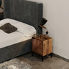 Lifestyle shot featuring the Nikita nightstand in a moody bedroom setting next to a dark gray tufted headboard with industrial lighting