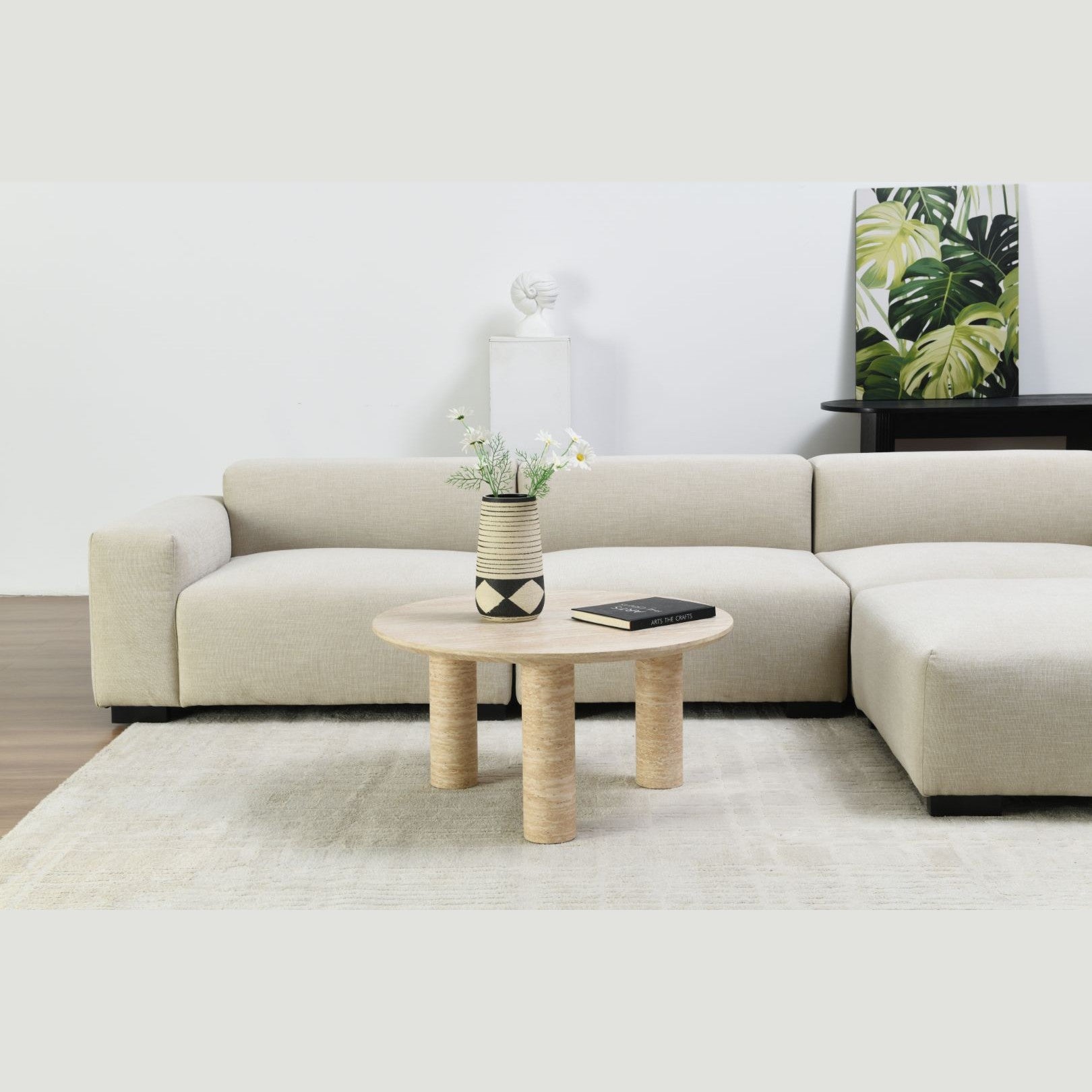 Wide lifestyle view showing the Nils coffee table centered on a neutral area rug with minimalist wall art in the background