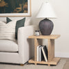 Lifestyle view showing the Nohr table styled as a side piece next to a white sofa with books stored on the lower shelf