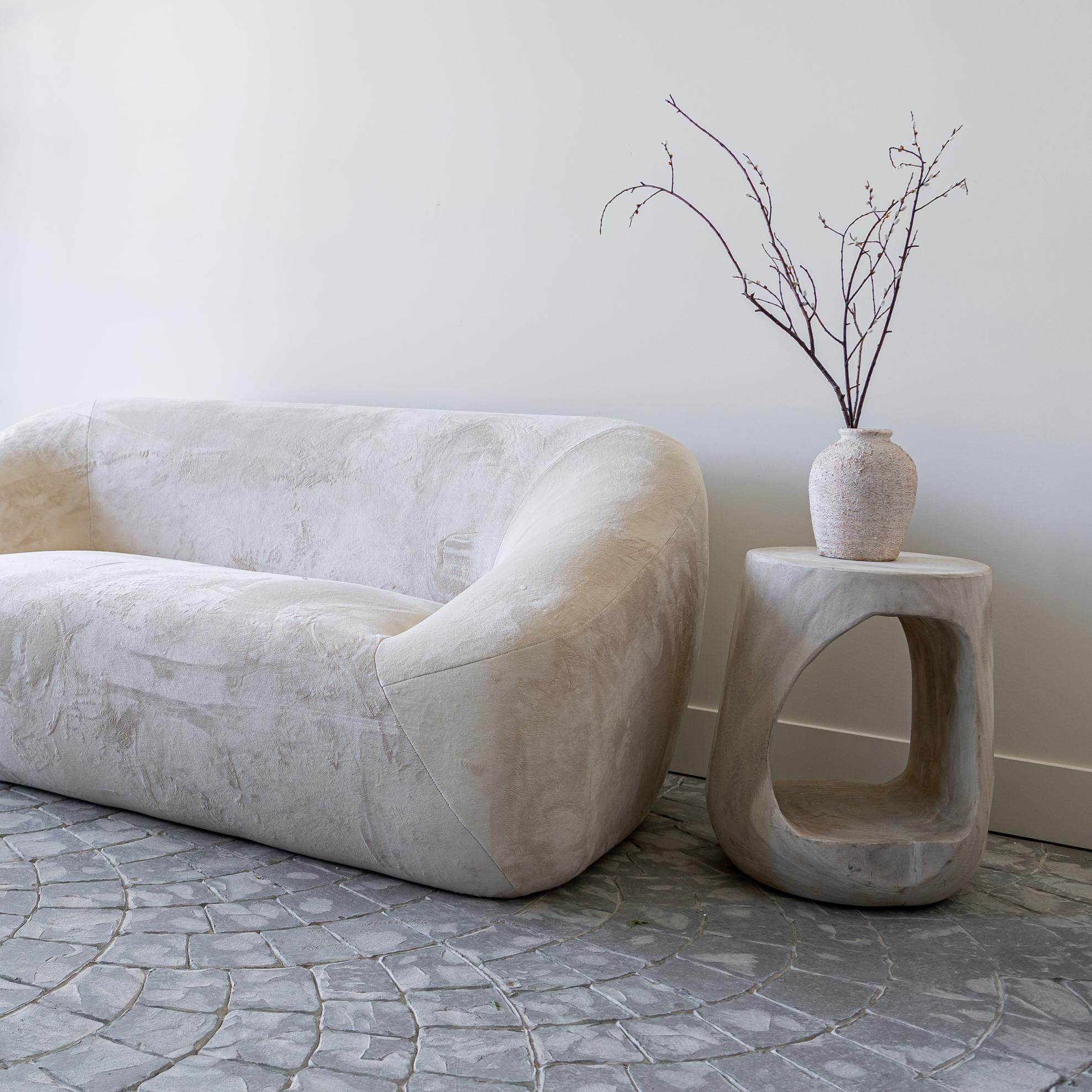 Wide lifestyle view showing the Nova Drift end table positioned next to a curved modern sofa to demonstrate scale