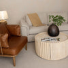 Lifestyle shot of the coffee table styled with a black vase and greenery in a bright minimalist interior