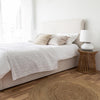Lifestyle shot featuring the Julia bed styled with neutral linens and a round jute rug in a bright master bedroom