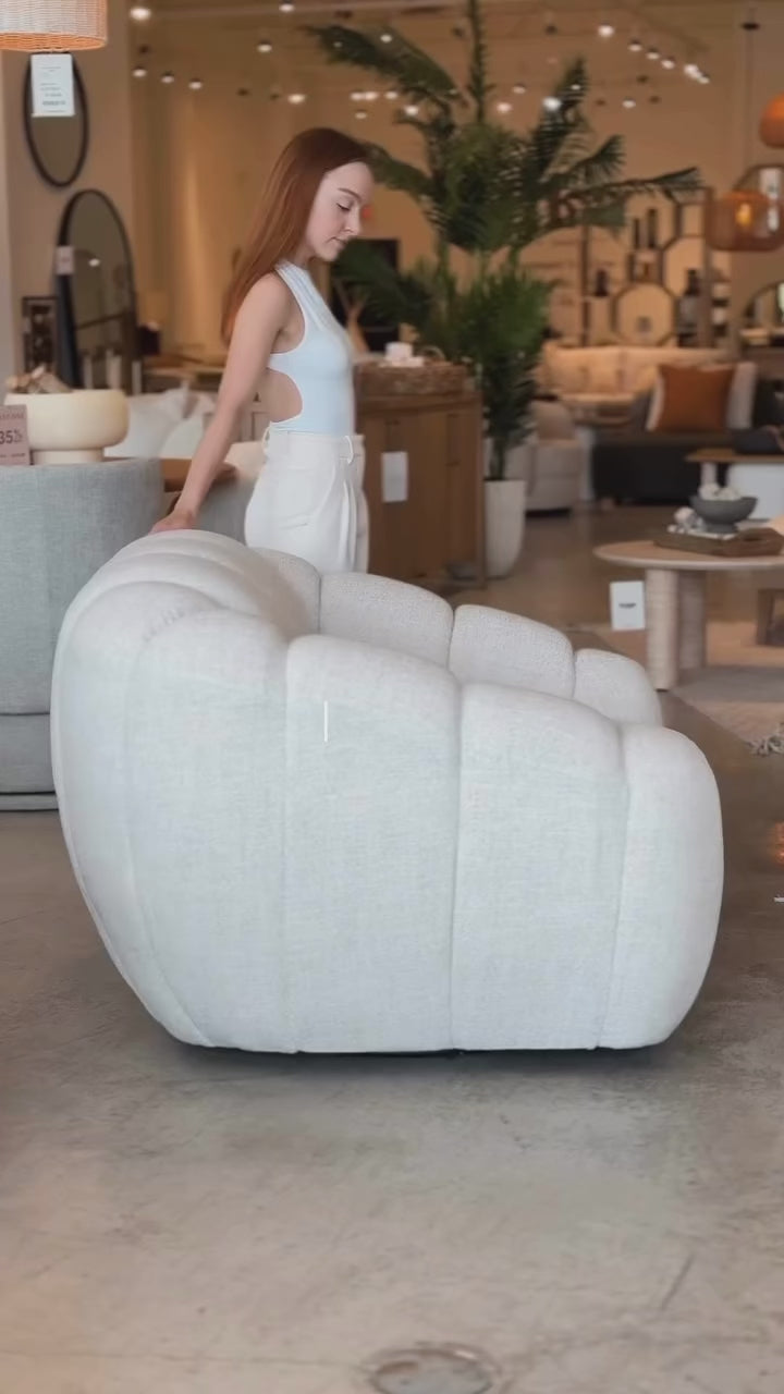 A person demonstrating the scale and 360-degree swivel functionality of the Riro Accent Chair in a showroom.