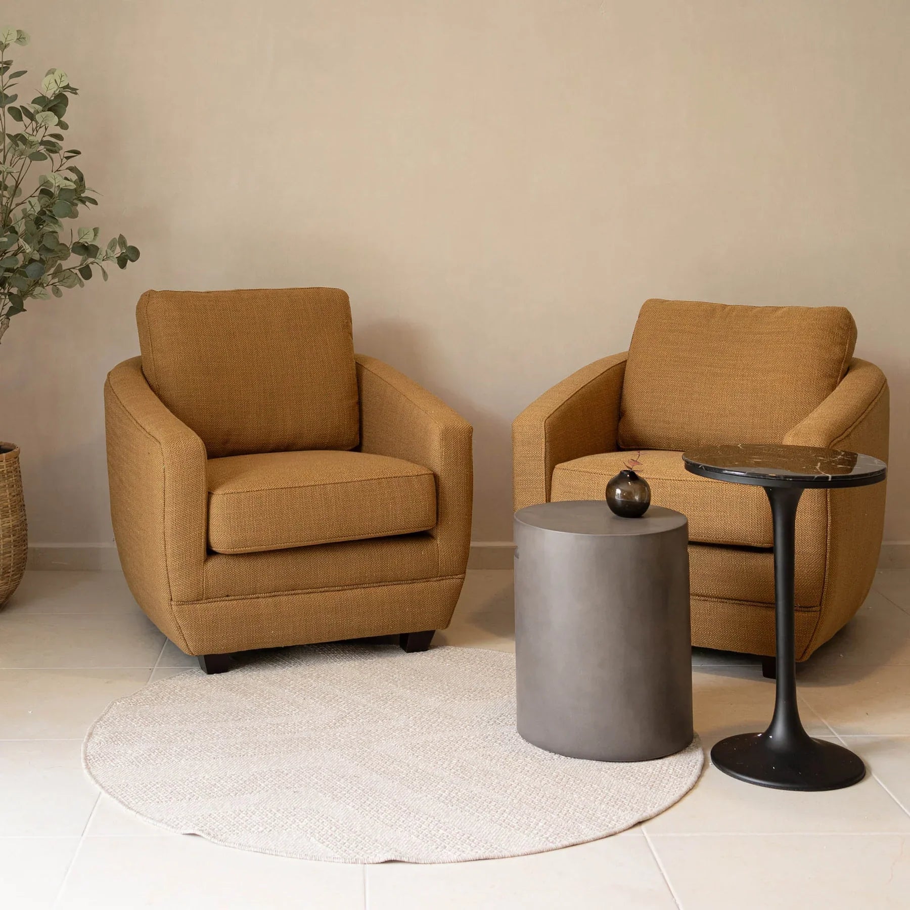 Lifestyle shot featuring the Primo table styled between two mustard yellow armchairs in a contemporary lounge setting