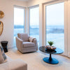 Wide lifestyle view showing the Primo coffee table centered in a bright contemporary room with large windows and a soft neutral rug