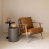 Lifestyle view of the Primo table used as a functional accent piece next to a tan leather armchair and grey cylindrical stool