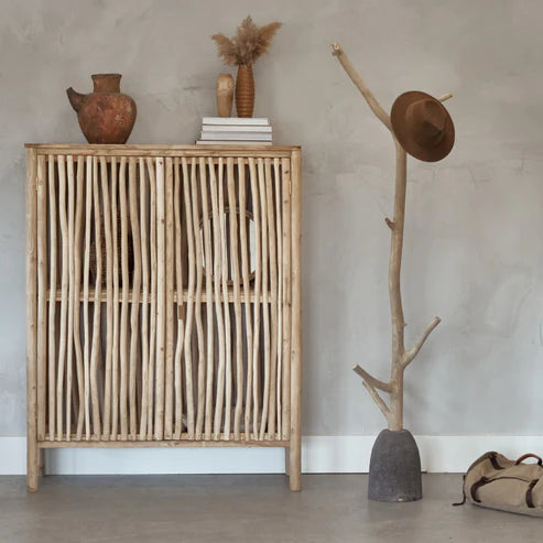 Lifestyle shot of an organic tree branch coat hook with a dark volcanic stone base styled in a rustic entryway with a matching wood cabinet