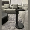 Close-up lifestyle shot highlighting the cantilevered design of the black metal side table tucked neatly against a grey textured sectional sofa