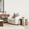 Lifestyle shot featuring the Rumer table styled next to a white bouclé armchair with books and home decor