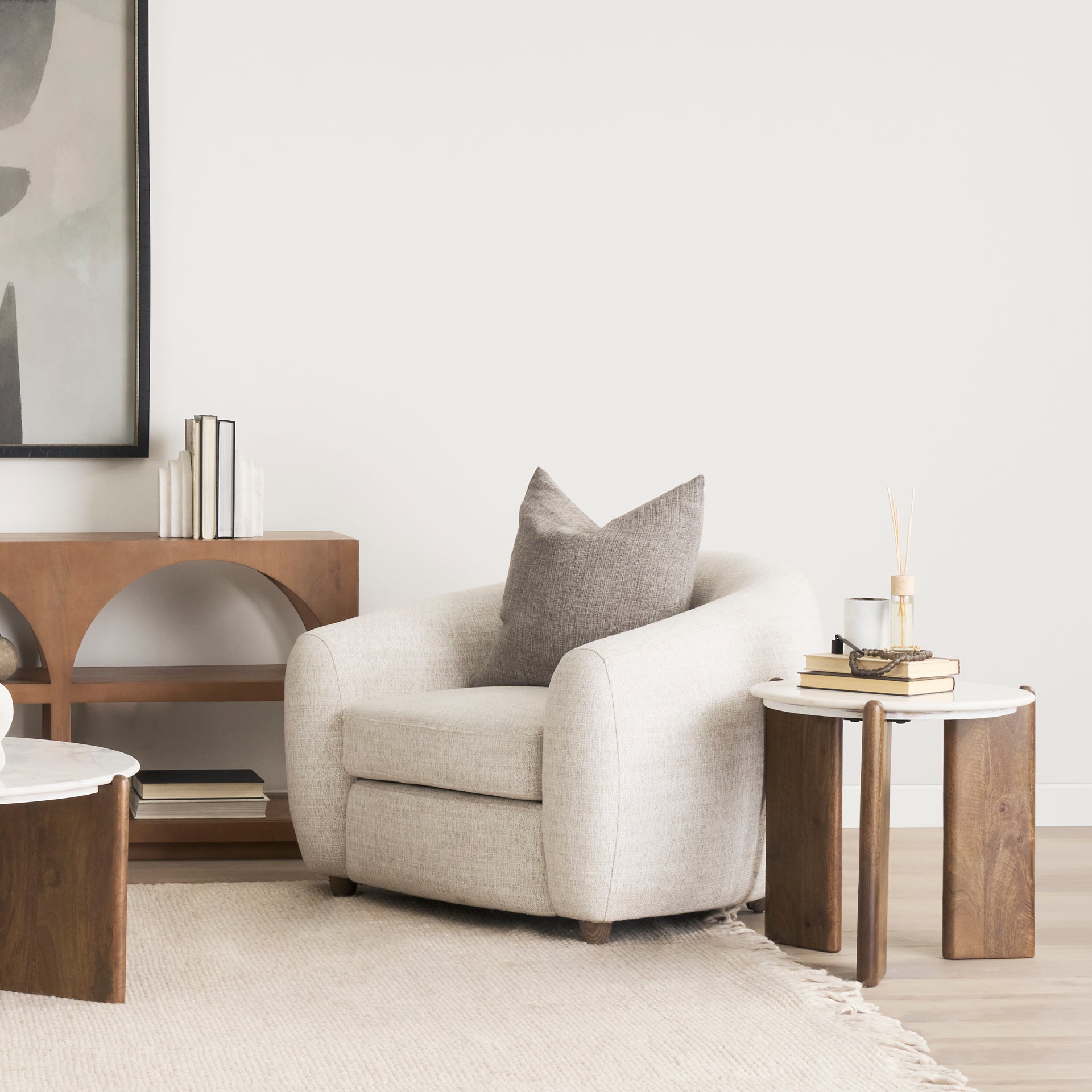 Lifestyle shot featuring the Rumer table styled next to a white bouclé armchair with books and home decor