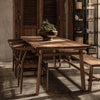 Moody lifestyle shot of the artisan dining table styled with matching wooden chairs and a bench in a warm rustic interior