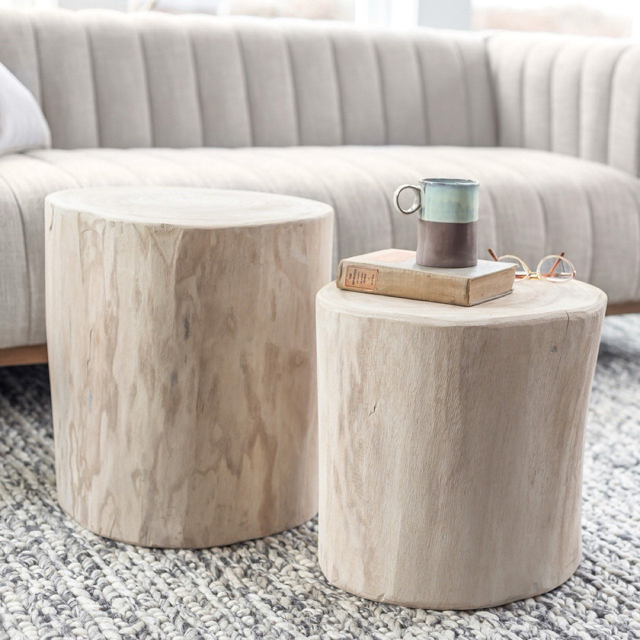Lifestyle view of the 18-inch white wood stump used as an accent table next to a sofa with books and a mug to demonstrate scale