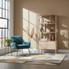 Lifestyle shot featuring the light oak bookcase styled with books and decor in a modern living room next to a teal velvet armchair