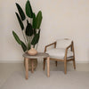 Lifestyle shot of the small round garden table styled with a modern wood accent chair in a bright outdoor or sunroom setting