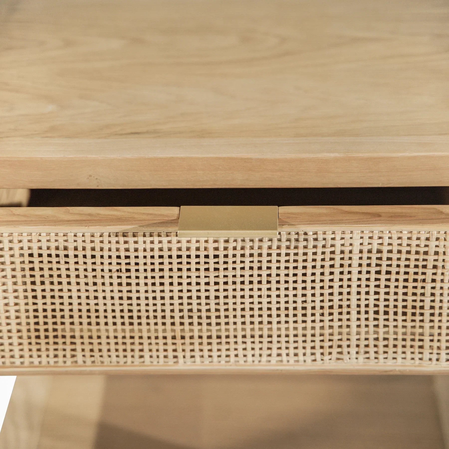 Straight-on front view showcasing the woven rattan drawer front and minimalist brass hardware on a light wood frame