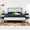 Lifestyle shot of the bed styled with navy and teal linens on a vibrant patterned rug in a modern bedroom