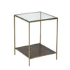 Three-quarter view of the Venus side table featuring a clear square glass top and a minimalist antique brass frame with a solid lower shelf