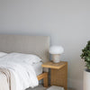 Lifestyle shot of the Luna walnut bed styled with white linens alongside a matching wood nightstand and modern lamp