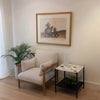Wide lifestyle shot demonstrating the table's scale when paired with a classic accent chair and wall art