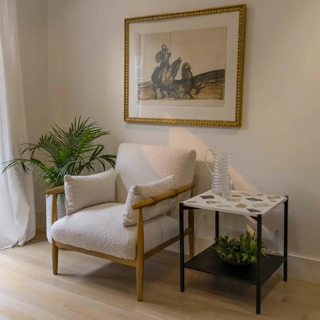 Three-quarter view of a square side table featuring a white mosaic terrazzo top and a black metal frame with a lower storage shelf