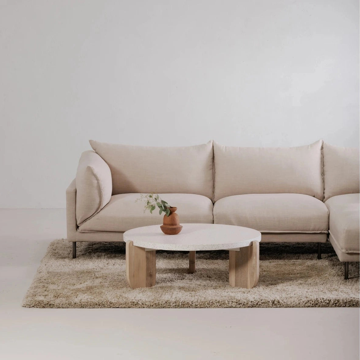 Front view of the Wunder coffee table featuring a thick circular white terrazzo top and three light wood sculptural legs