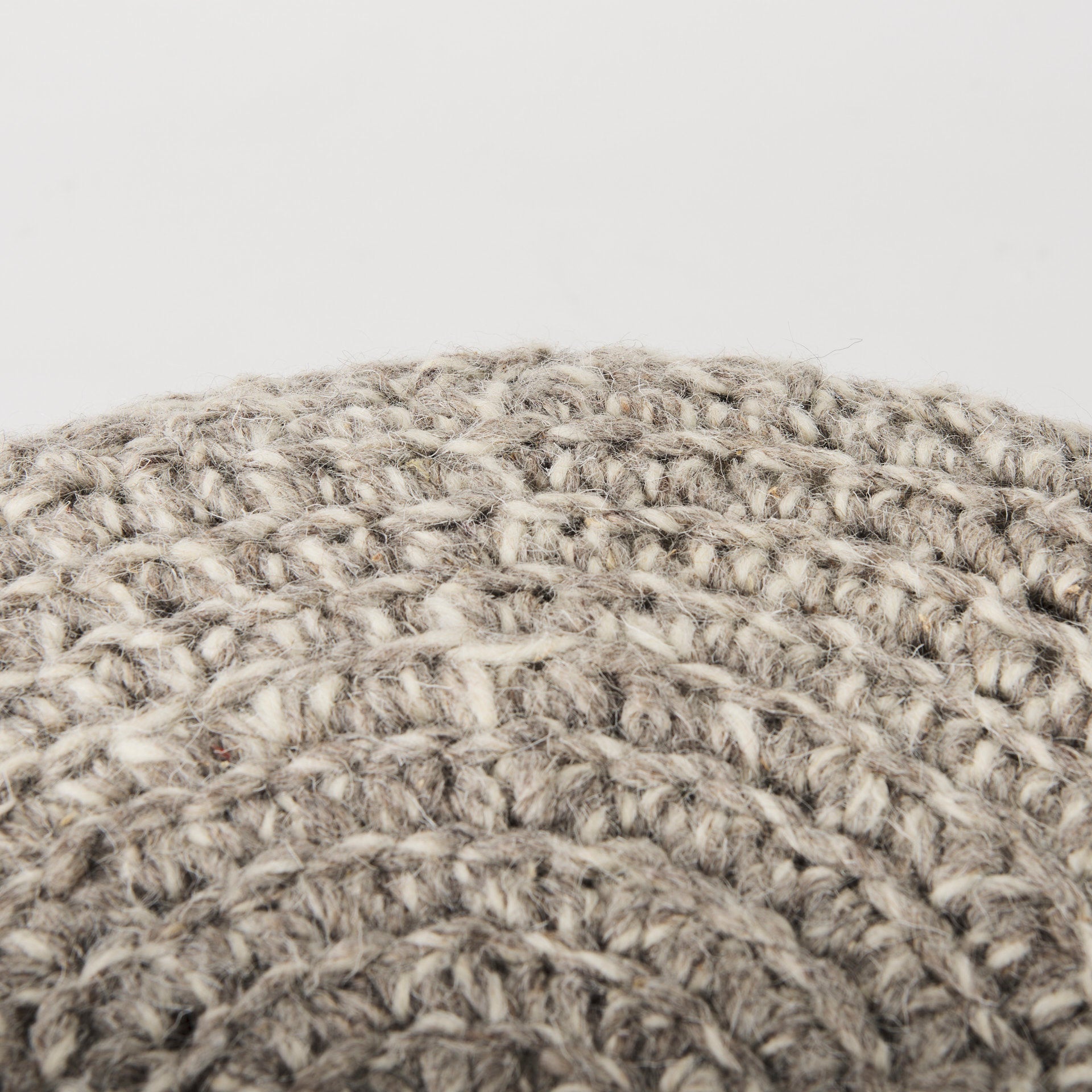 Front three-quarter view of the Bina accent stool featuring a thick gray knitted wool seat and four natural wood legs