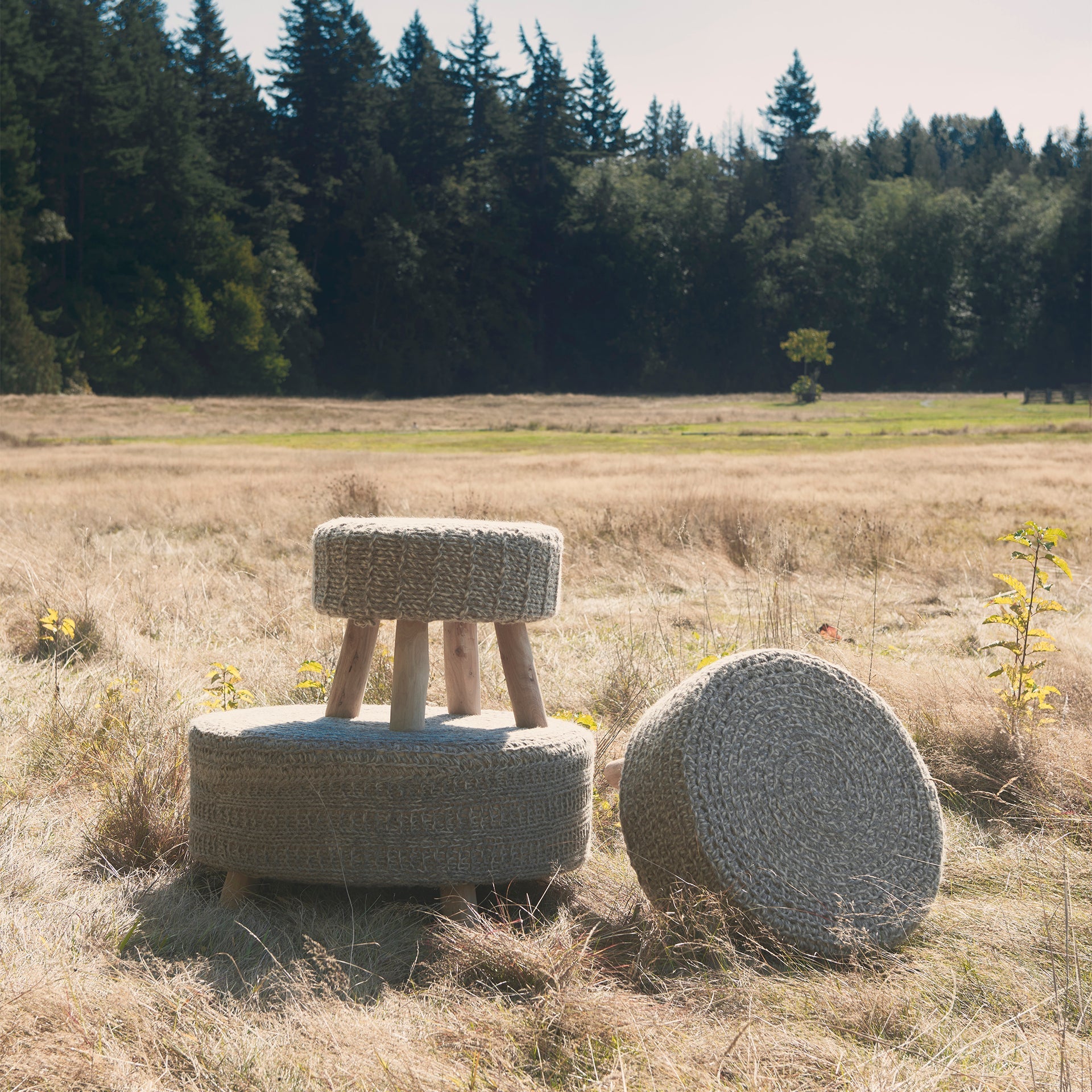 Front three-quarter view of the Bina accent stool featuring a thick gray knitted wool seat and four natural wood legs
