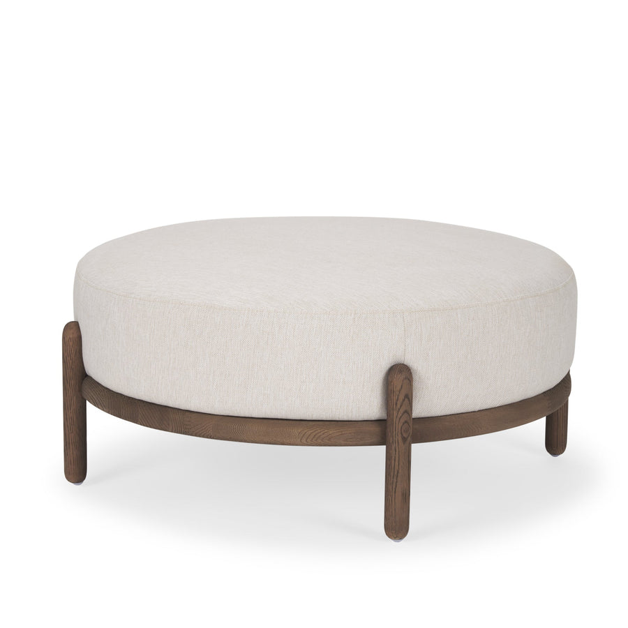 Front three-quarter view of the Gwynn ottoman featuring a cream upholstered seat and a curved oak wood frame