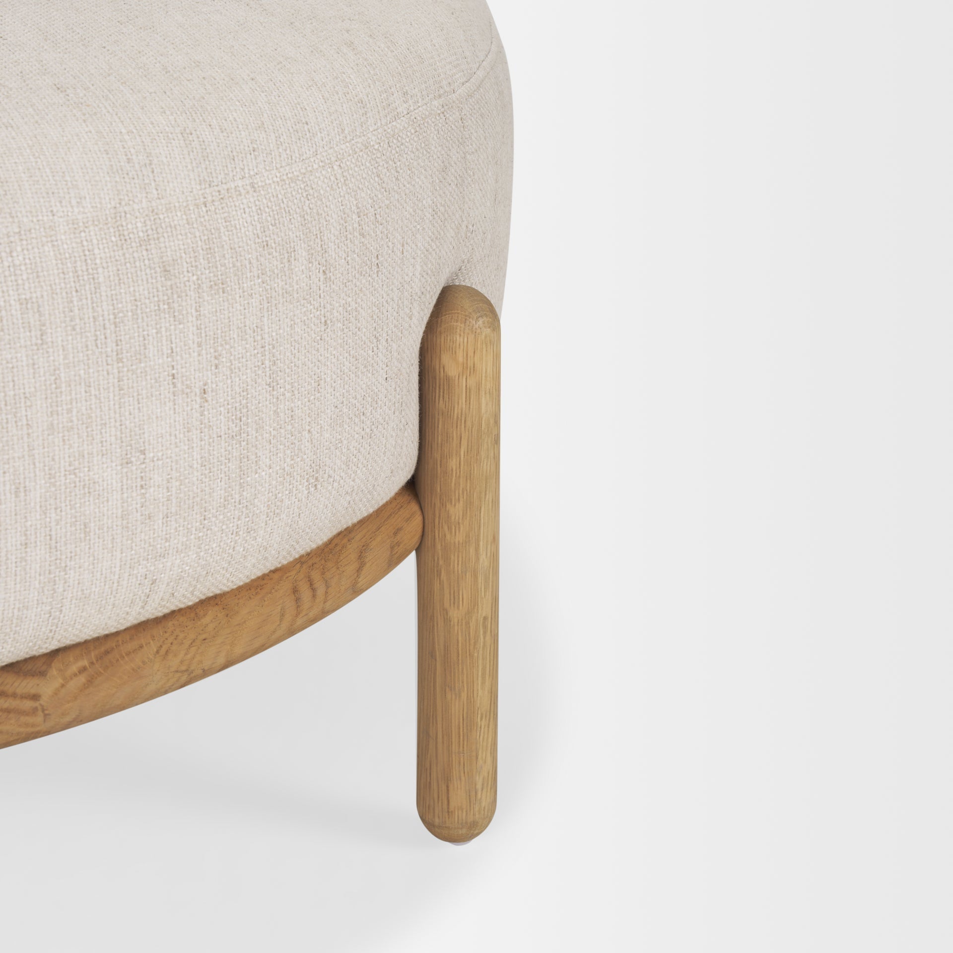 Front three-quarter view of the Gwynn ottoman featuring a cream upholstered seat and a curved oak wood frame