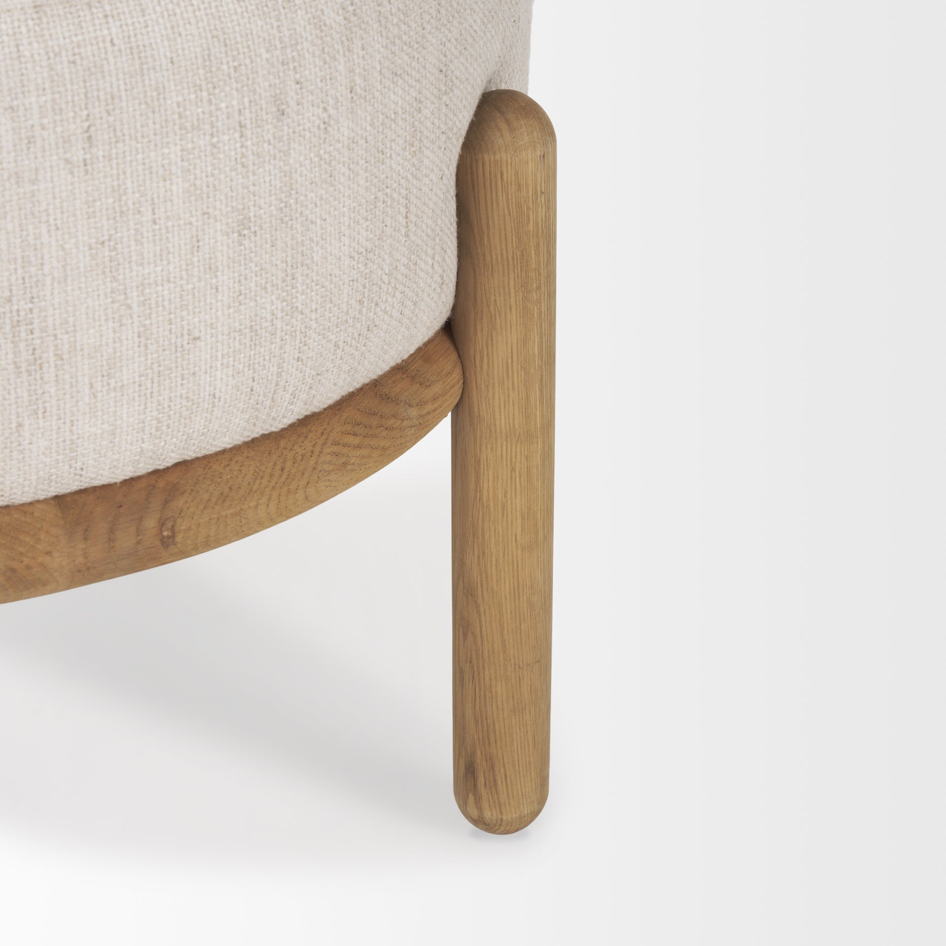 Front three-quarter view of the Gwynn pouf featuring a cream upholstered seat and a curved oak wood frame