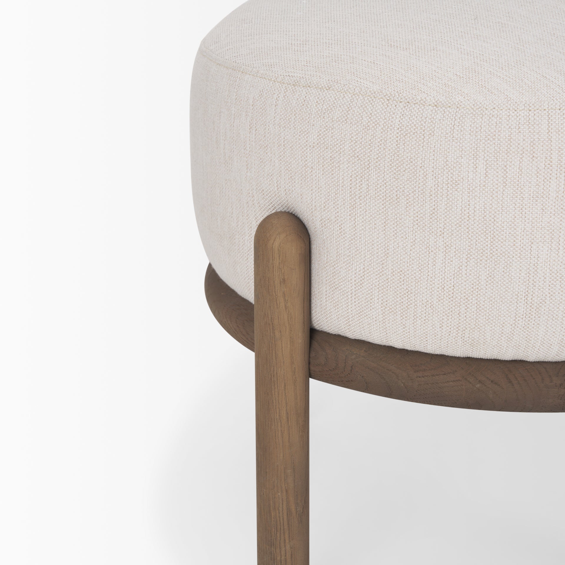 Front three-quarter view of the Gwynn pouf featuring a cream upholstered seat and a curved oak wood frame