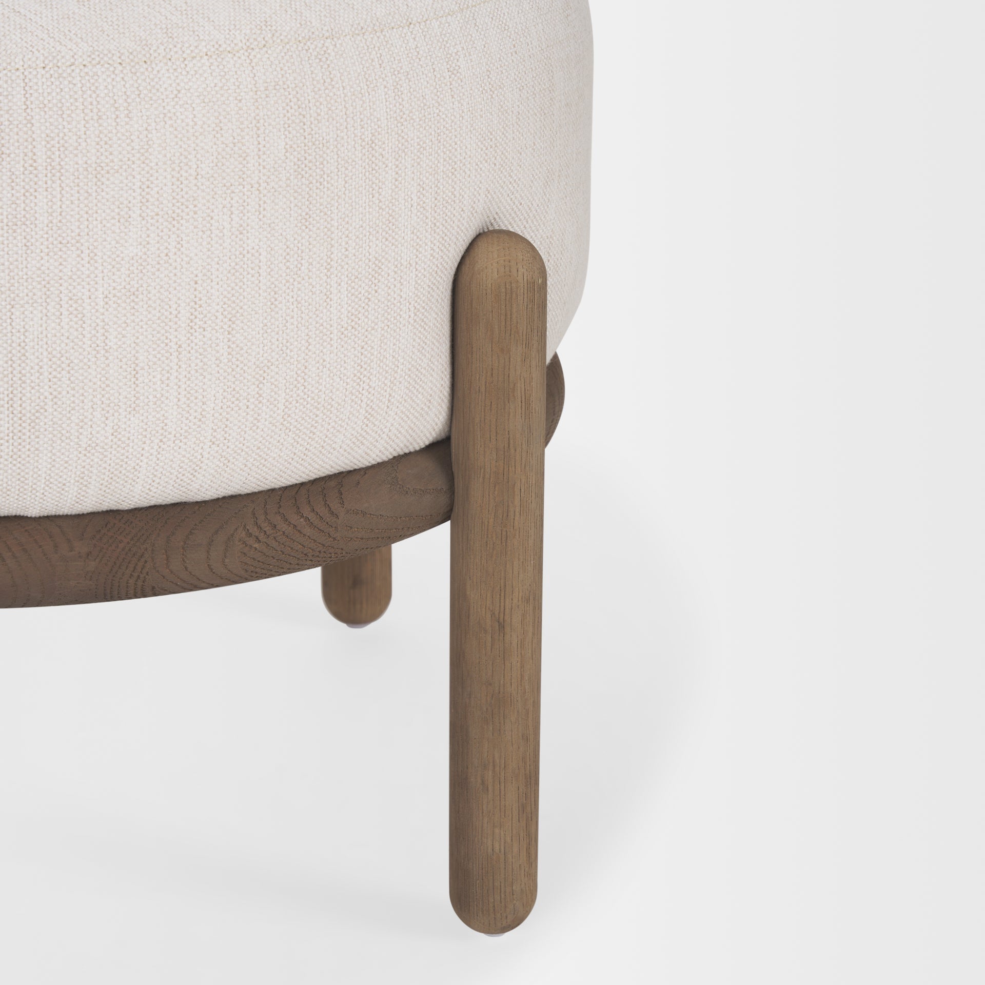 Front three-quarter view of the Gwynn pouf featuring a cream upholstered seat and a curved oak wood frame